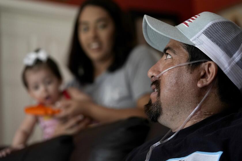 Freddy Fernandez sits with his fiancé, Vanessa Cruz, and their 8-month-old daughter, Mariana Fernandez in their home Friday, June 10, 2022, in Carthage, Mo. After contracting COVID-19 in August 2021, Fernandez spent months hooked up to a respirator and an ECMO machine before coming home in February 2022 to begin his long recovery from the disease. (AP Photo/Charlie Riedel)