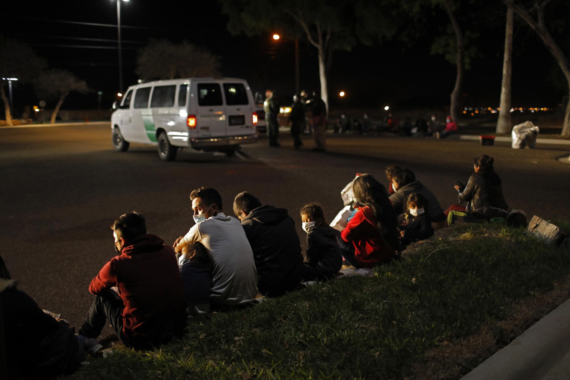 Several asylum seekers sit on a curb.