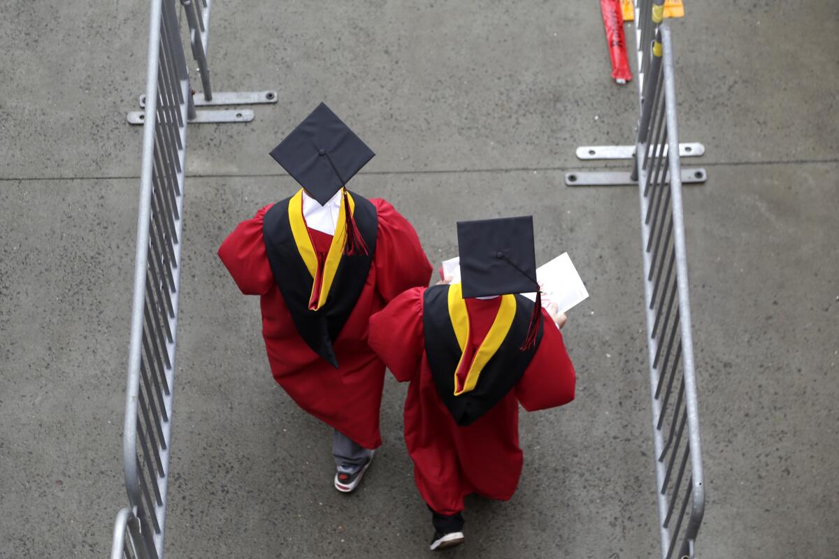 New graduates in red robes walk between metal barriers