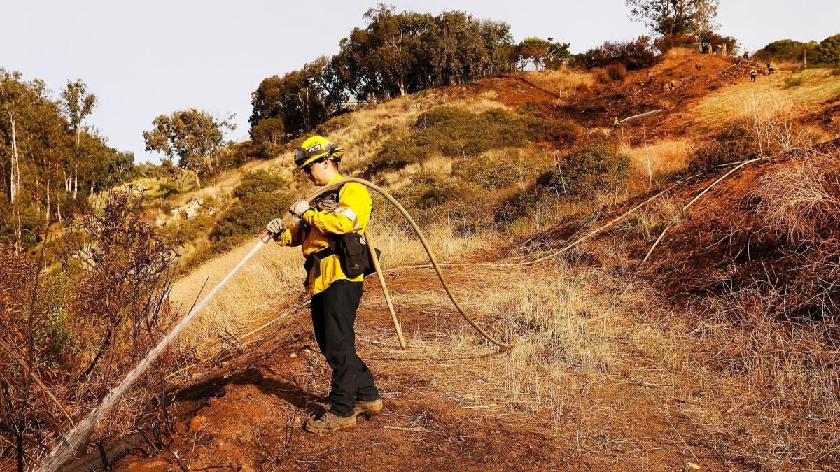 Los Angeles County Firefighter Jake Whiteaker douses hot spots on a scorched hillside in Malibu.