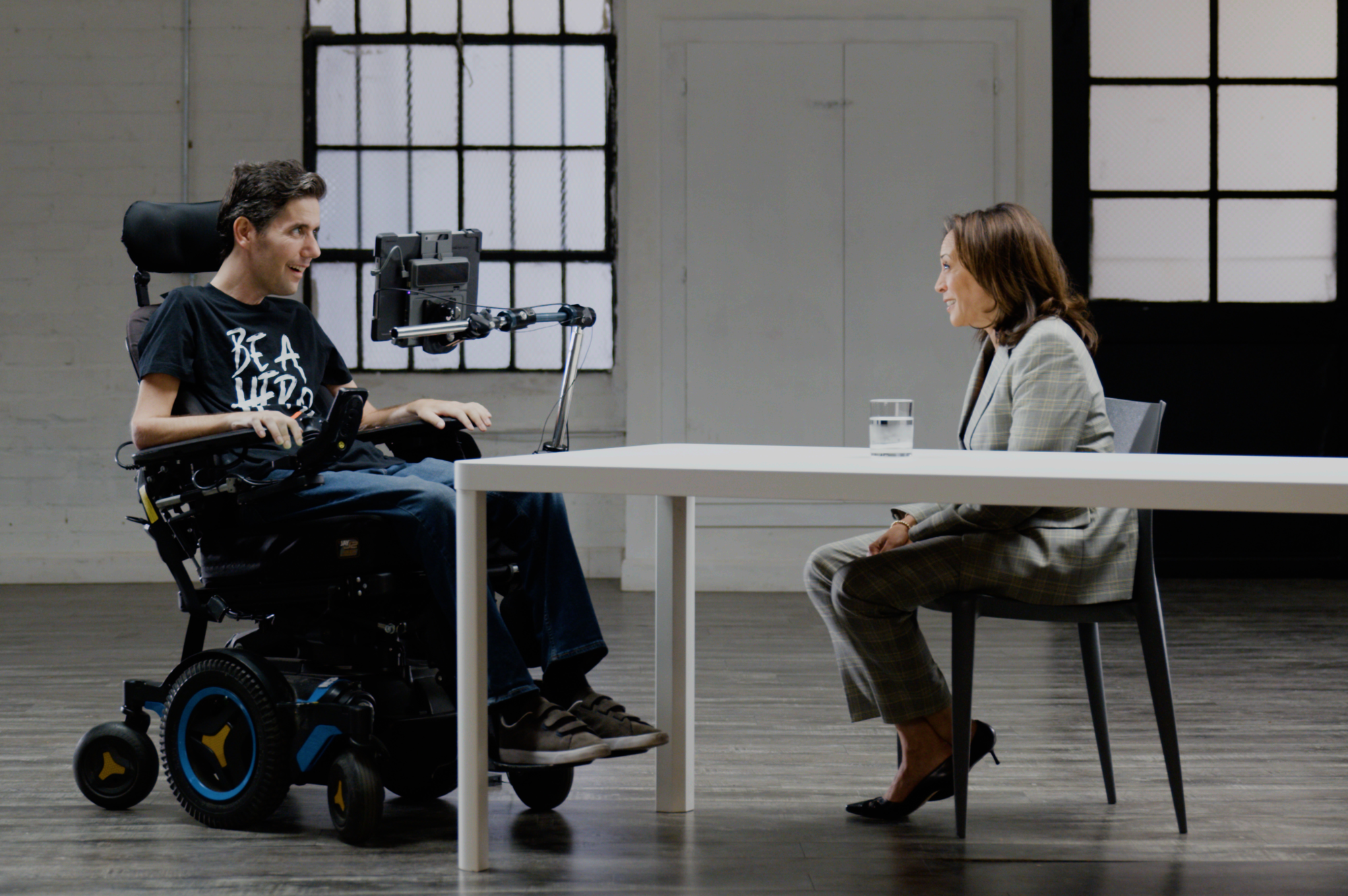 A man in a wheelchair faces a woman seated at a table.
