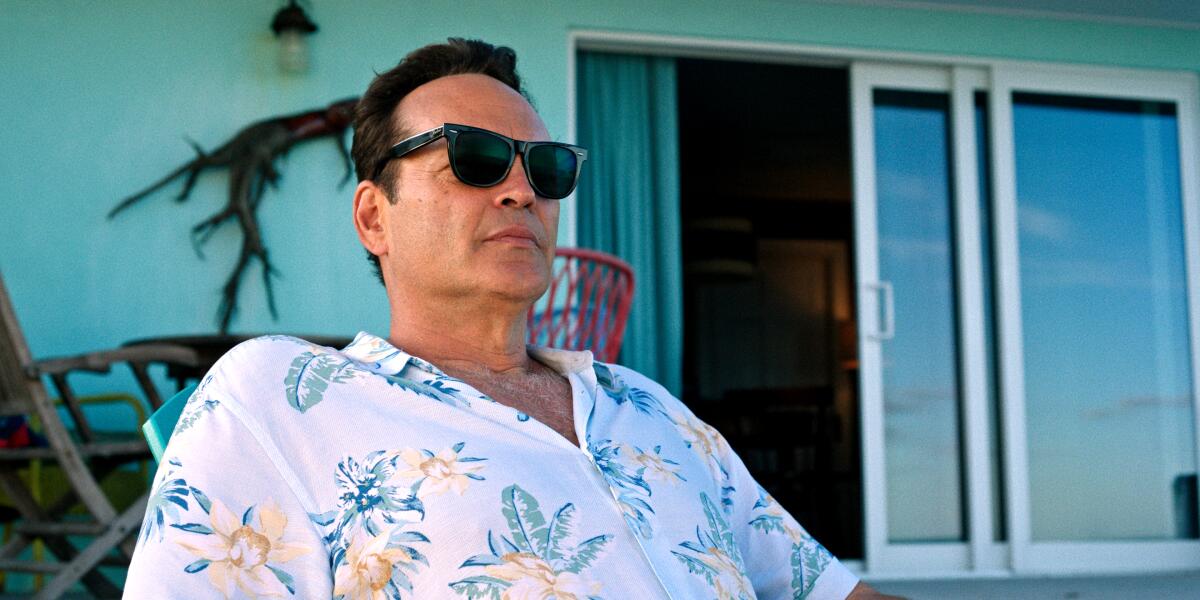 A man wearing sunglasses and a Hawaiian shirt sitting on a back porch.