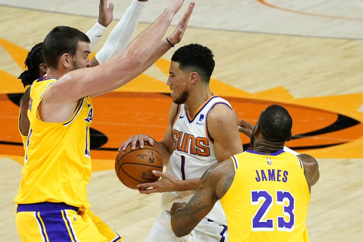 Lakers center Marc Gasol, left, and forward LeBron James pressure Suns guard Devin Booker during a drive on Dec. 18, 2020.
