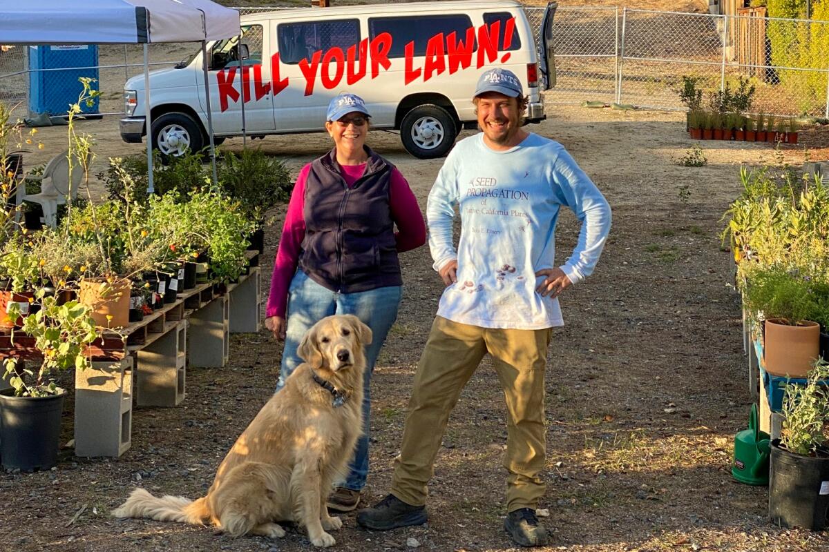 Two people and a dog next to some plants and in front of a van that reads Kill Your Lawn! 