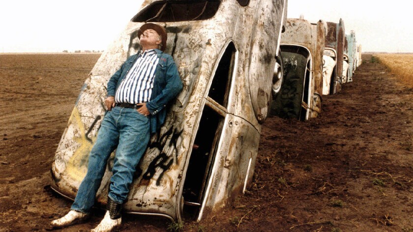 Stanley Marsh III, shown here leaning leans on one of the 10 Cadillacs buried down on his ranch west of Amarillo, Texas, has died.