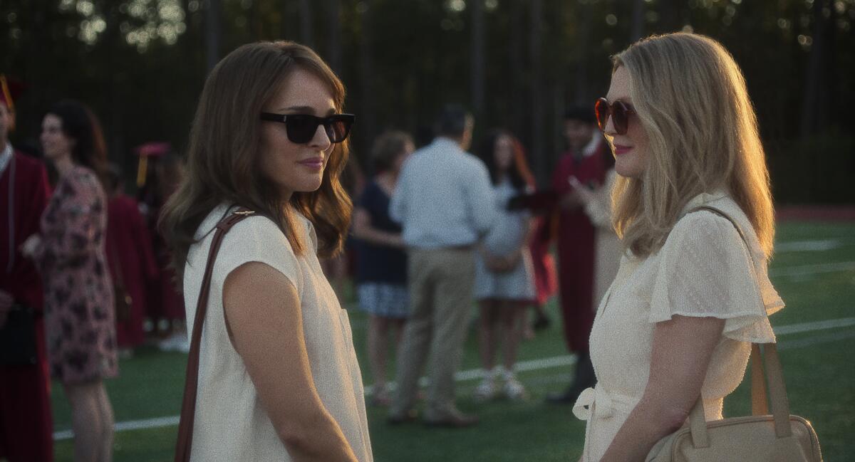 Two women in shades converse on a lawn.