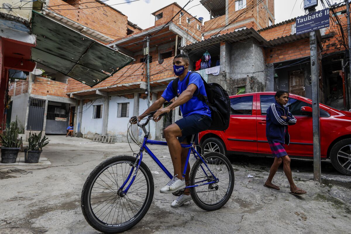 Logistics company Favela Brasil Xpress deliveryman Jonathan Arcanjo, cycles through alleys to deliver orders in the Paraisopolis favela of Sao Paulo, Brazil, Tuesday, Aug. 31, 2021, amid the COVID-19 pandemic. Favela Brasil Xpress, a startup created six months ago, reached the milestone of 100,000 packages delivered in areas that are not properly served by the postal service or by traditional transport and delivery companies, while ensuring the arrival of food, medicine and home supplies to people in the community. (AP Photo/Marcelo Chello)