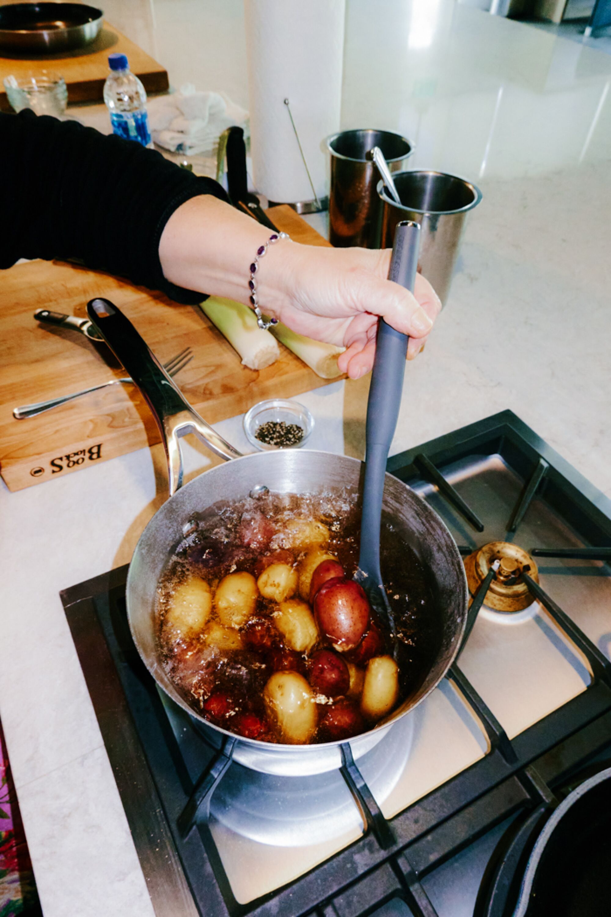 A hand stirs potatoes in a pot.