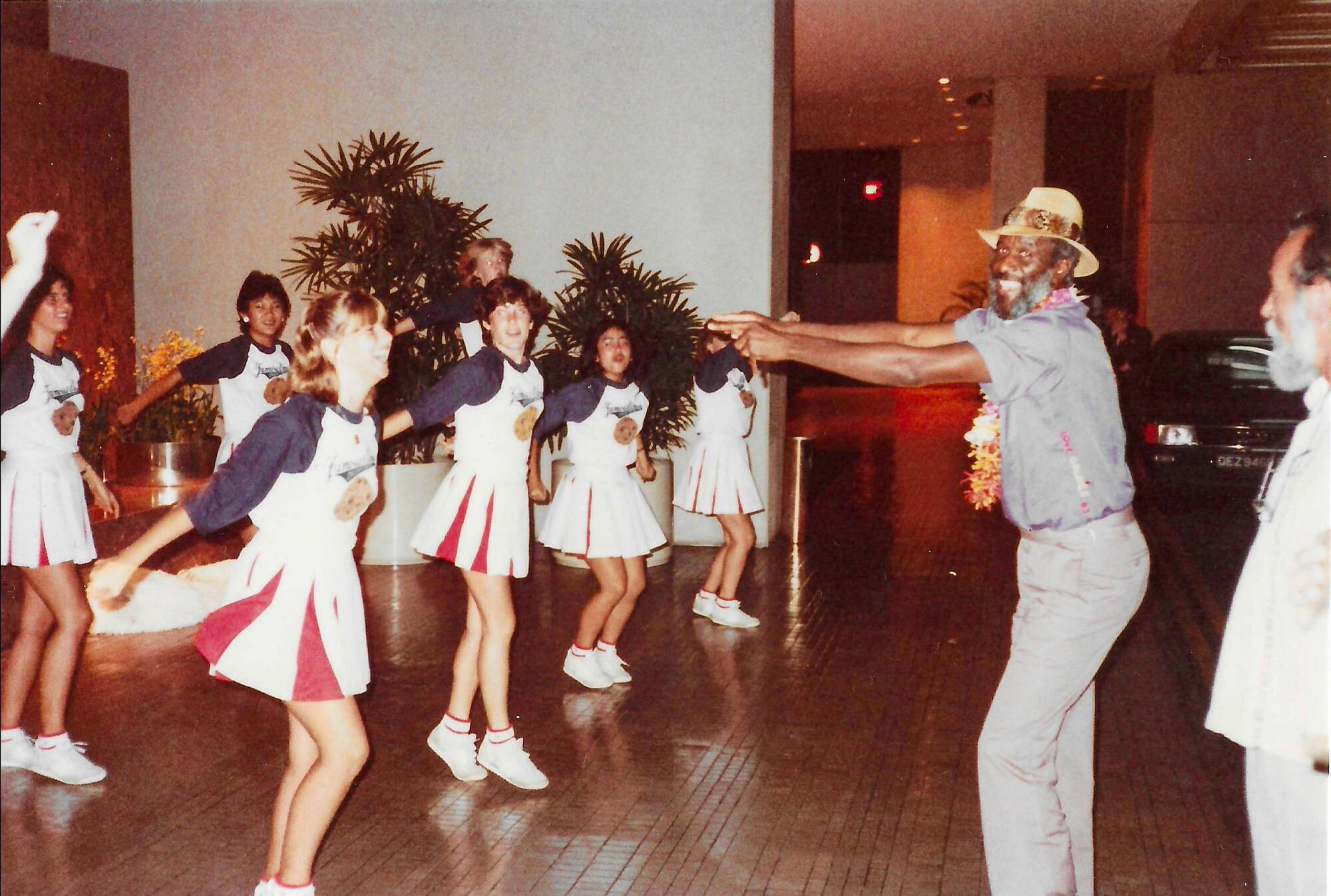 Wally Amos dances with cheerleaders wearing Famous Amos cookie T-shirts.