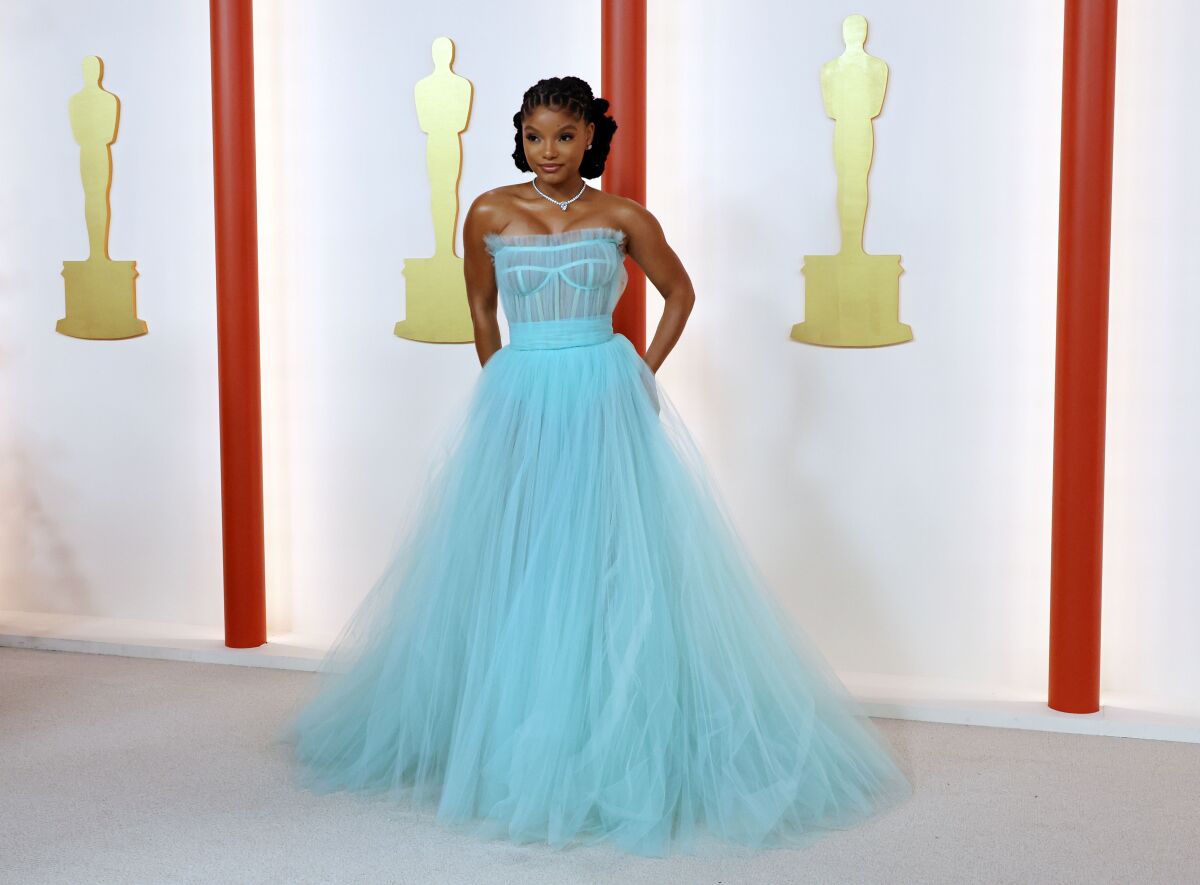A woman in a long blue gown poses on a champagne carpet.