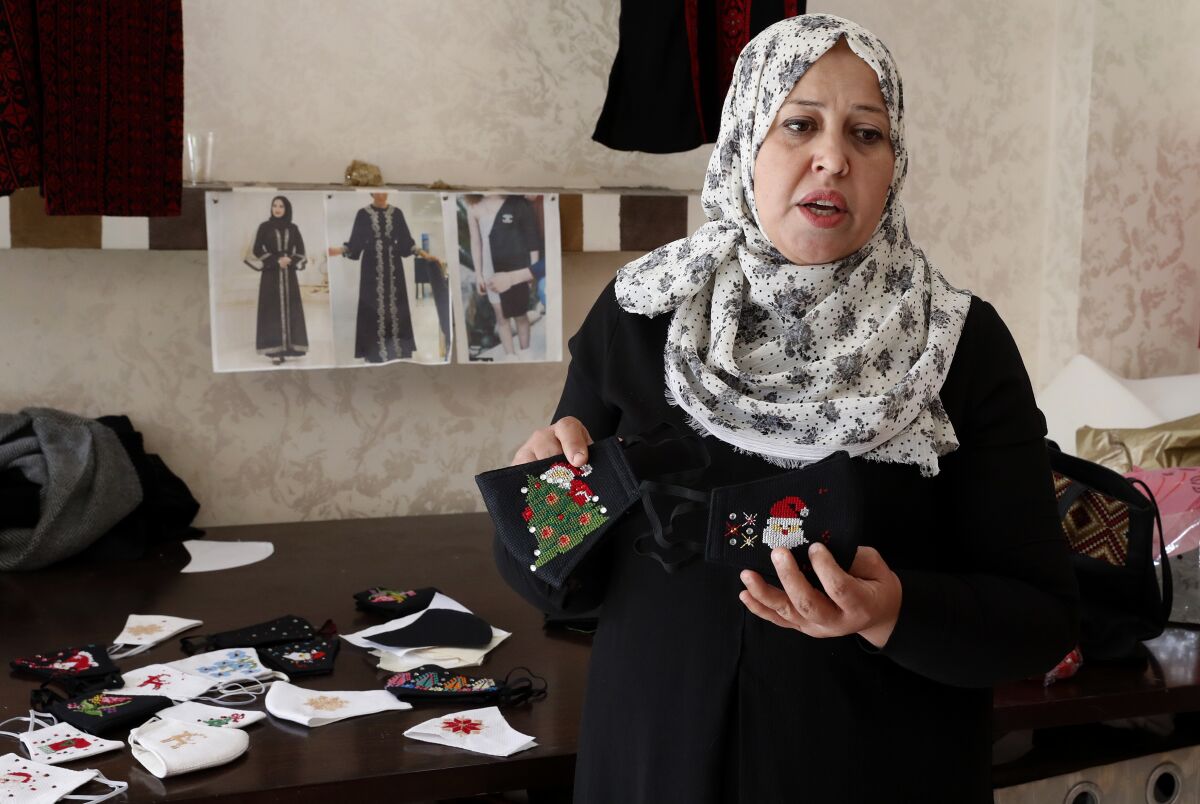 Suhad Saidam, shows stitched images of Santa Claus and Christmas on face masks at her sewing workshop in Gaza City, Monday, Dec. 14, 2020. In the blockaded Gaza Strip, the Christmas season is giving a boost to Saidam's business that produces pandemic face masks decorated with holiday symbols. They also have provided a small boost several dozen families in a Palestinian enclave run by the Islamic militant Hamas group. (AP Photo/Adel Hana)