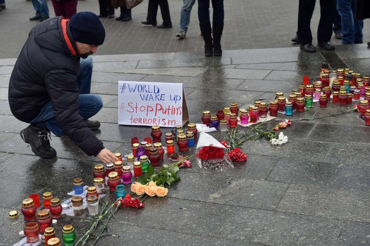 A man sets a candle near placard reading "World wake up. Stop Putin's terrorism" on Independence Square in Kiev, during a rally for people who died as a result of shelling in the southern Ukrainian city of Mariupol.