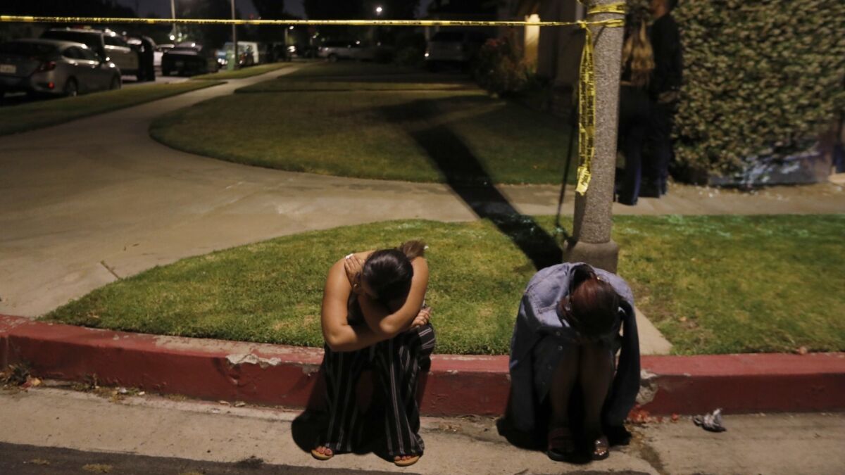 Two young women sit near crime tape on West Tiara Street in North Hollywood, where several people were shot at a house party. Two suspects have been taken into custody.