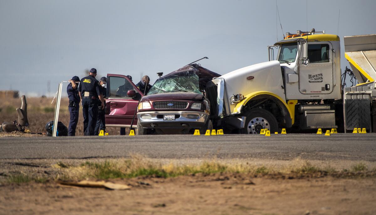 A damaged SUV sits on a road in front of a big rig with emergency personnel nearby.