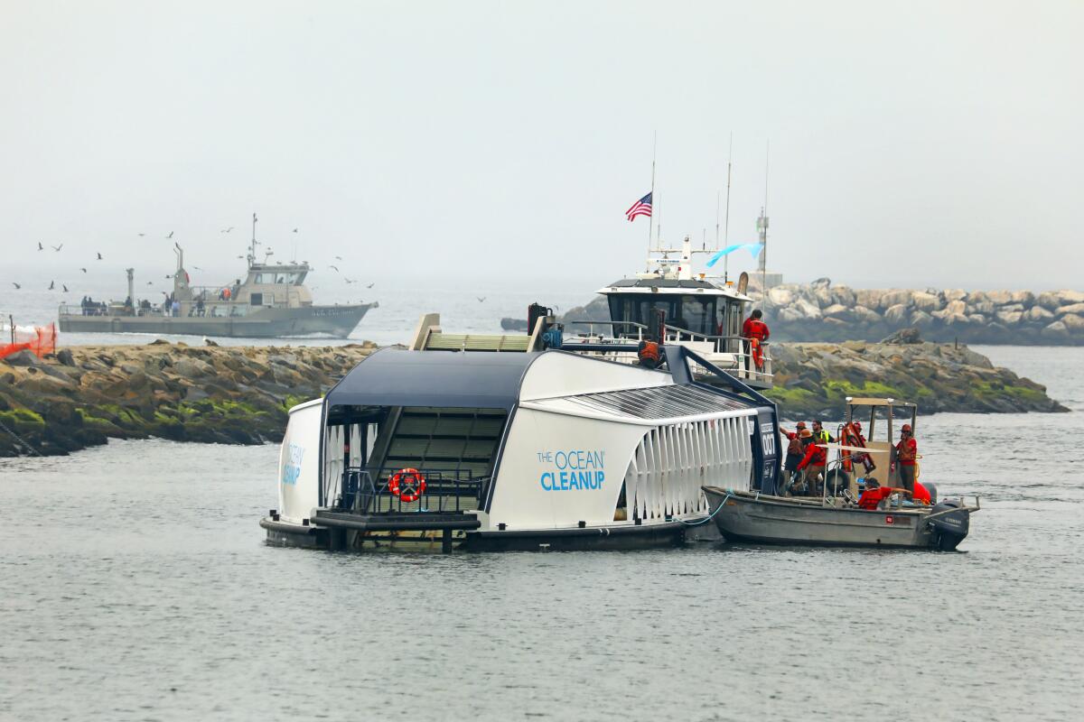The Ballona Creek Trash Interceptor floats in the water while boats are in the background.