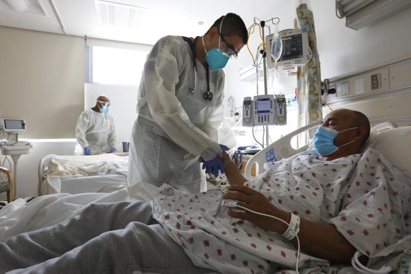 Los Angeles County, California-Dr. Jeison Recinos, of internal medicine checks on Jose Luis Andrade Moscoso, age 52, who is suffering from COVID-19 in one of the covid wards at Olive View-UCLA Medical Center on Jan. 11, 2020. Moscoso doesn't know how he got COVID-19. Supervising RN Mesfin Meshesha, left, cares for another COVID patient in the same room. Olive View-UCLA Medical Center is a hospital, funded by Los Angeles County, located in the Sylmar neighborhood of Los Angeles, California. It is one of the primary healthcare delivery systems in the north San Fernando Valley. (Carolyn Cole / Los Angeles Times)