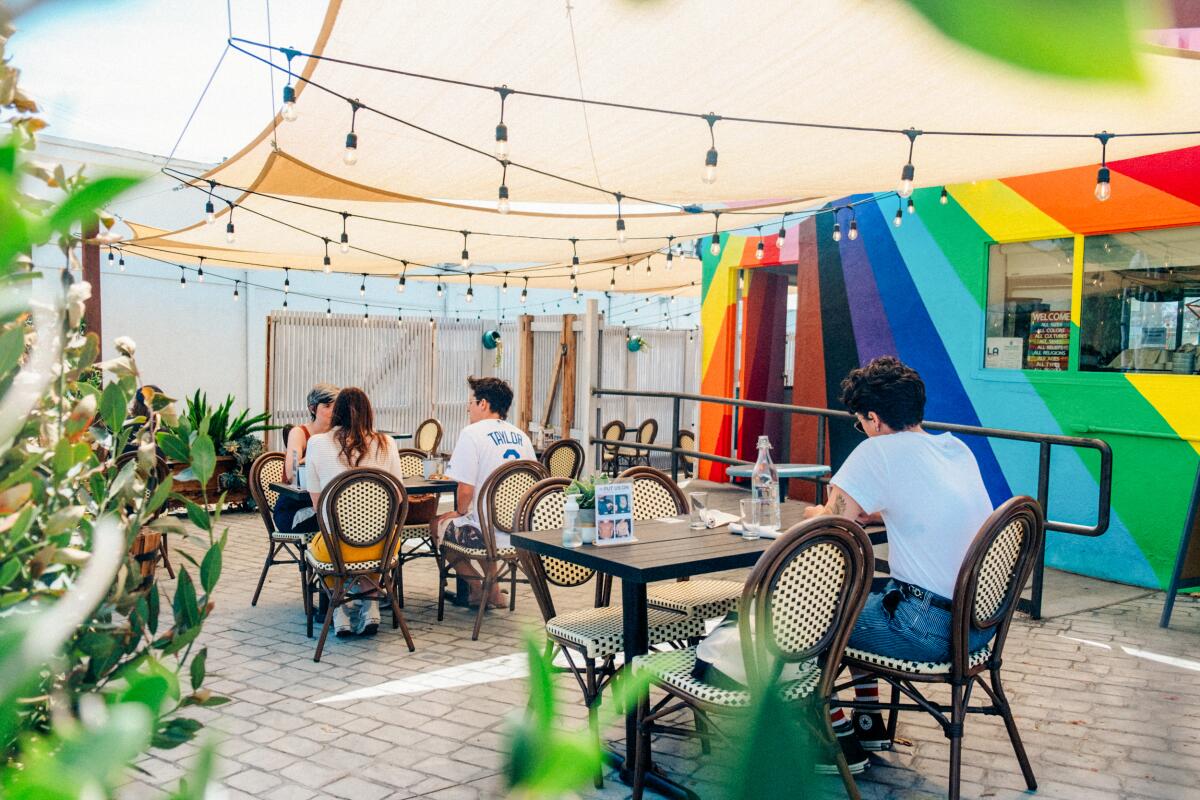 A restaurant patio under lights and shade cloth, with a rainbow mural on one wall