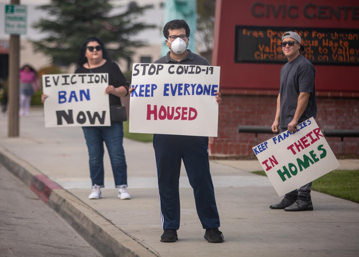 People on a sidewalk hold signs, including one that says, "Stop COVID-19. Keep everyone housed." 