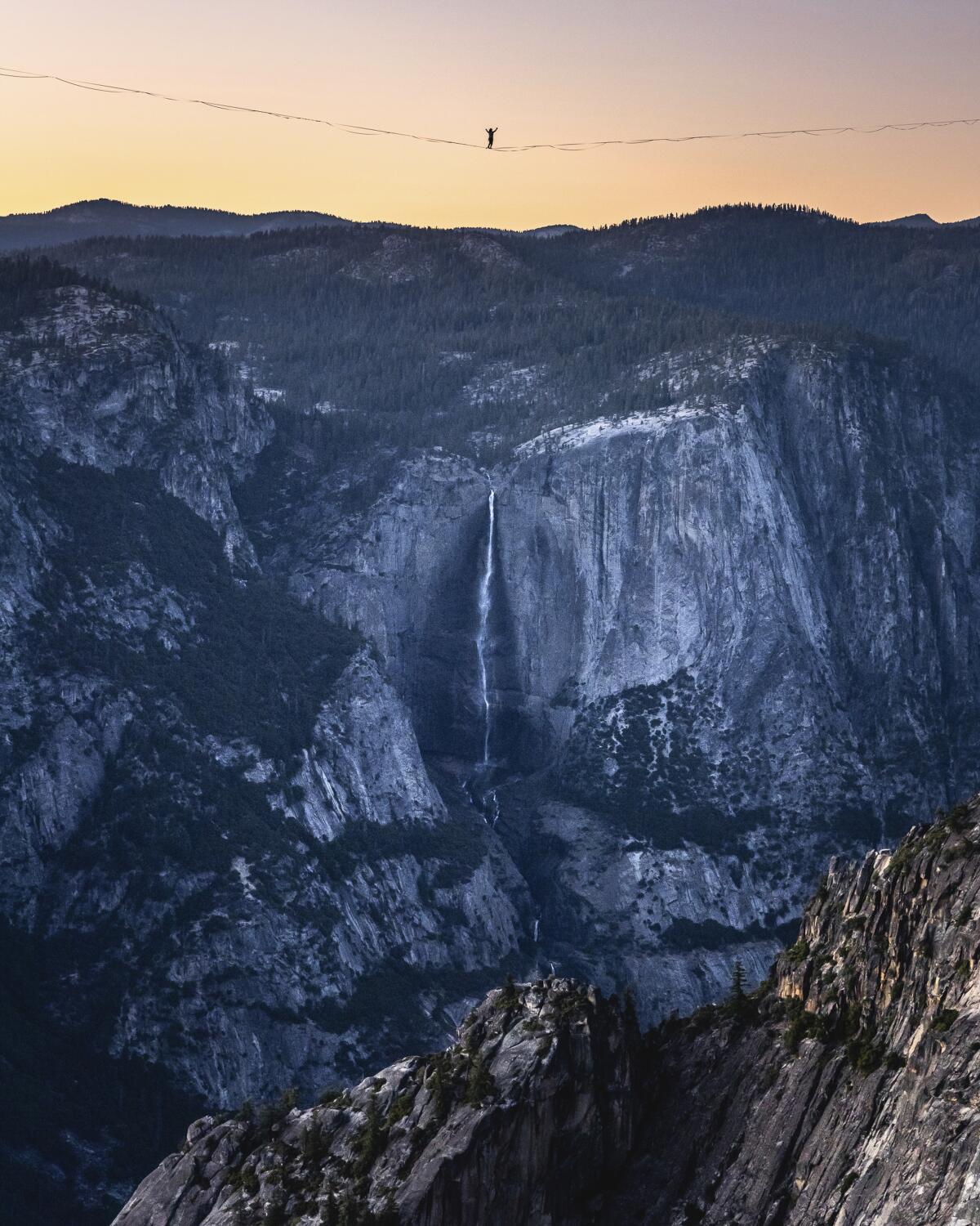 A person is viewed from afar standing in the middle of a line suspended above a rocky cavern.