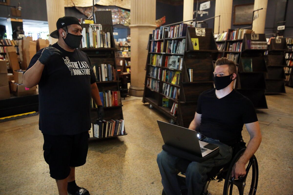 Jose "Shrek" Navarro, left, chats with Josh Spencer, right, while preparing custom orders for customers in the Last Bookstore.