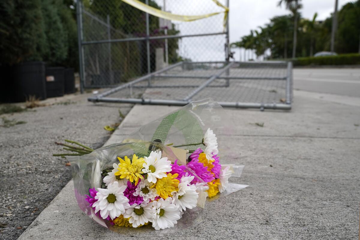 A bouquet of white, pink and yellow flowers in plastic lies on the sidewalk next to a fallen fence.