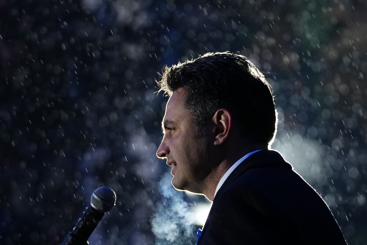 A man speaks into a microphone in the rain as lights shine on him at night