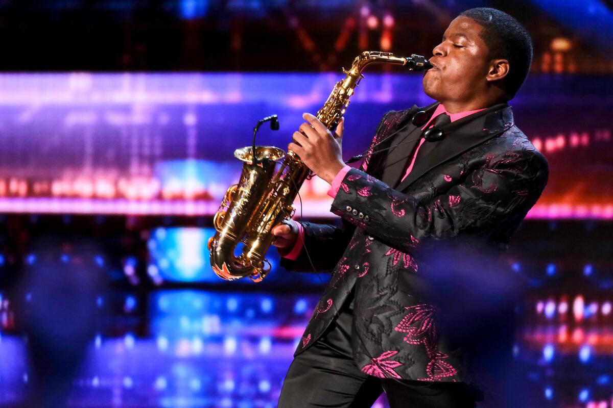 A man in a black suit with pink flowers plays the saxophone 
