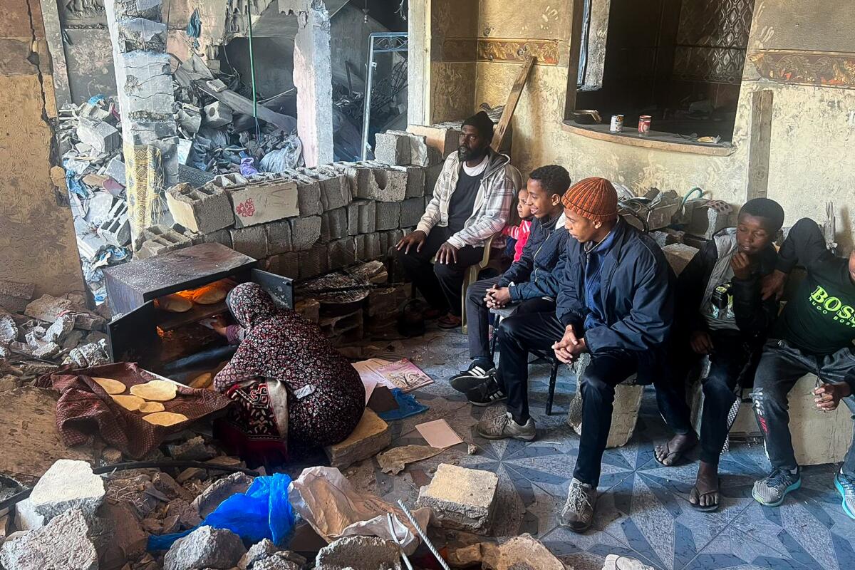 A family sits in a home whose walls were damaged or knocked out in a bombing