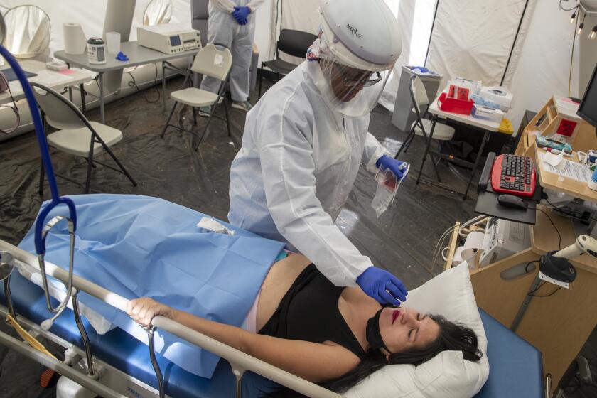 MISSION HILLS, CA - JULY 10: Nurse Janil Wise (CQ), left, inserts a nasal swap during a COVID-19 test for patient Sarah Bodle, who is 31 weeks pregnant, in the OB triage tent at Providence Holy Cross Medical Center on Friday, July 10, 2020 in Mission Hills, CA. (Brian van der Brug / Los Angeles Times)