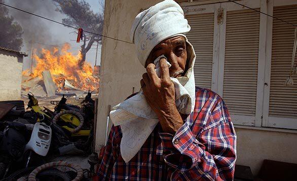 A man wipes his eye in front of his home in Dioni, 25 miles east of Athens, as a fire burns nearby. An overnight drop in gale-force winds offered hard-pressed Greek firefighters a brief respite Monday after wildfires raged unchecked for two days north of the capital, burning houses and swaths of forest while forcing thousands to flee their homes.