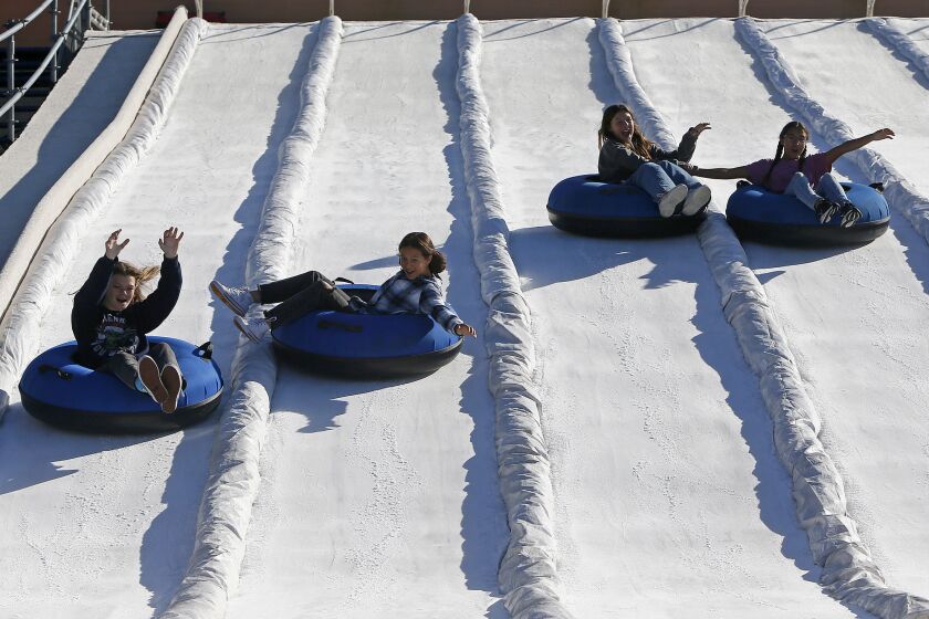 Orange County residents, left to right, Haylee Hanks, 14, Lacy Duckwitz, 14, Ava Williams, 12, and Lily Duckwitz, 12, glide down a snow slide during a sneak preview of Winter Fest OC on Wednesday at the OC Fair & Event Center in Costa Mesa. (Kevin Chang / Daily Pilot)