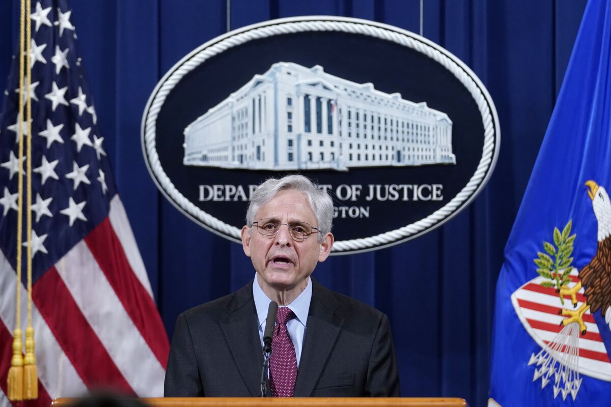 Merrick Garland speaks at a podium, a "Department of Justice" sign and flags behind him.