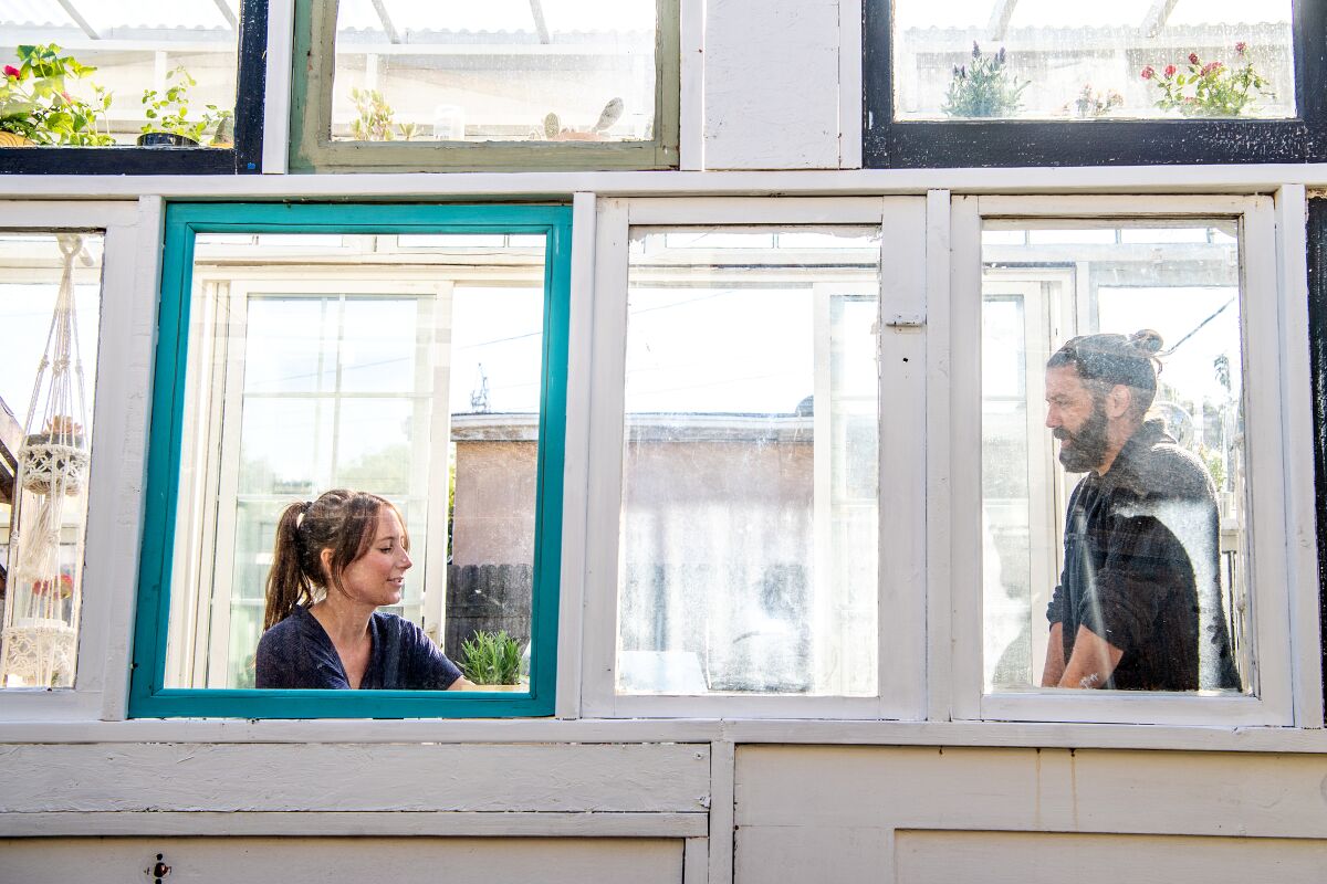 Jenny Grosso and Trevor Morris are framed like portraits in windows of their greenhouse.