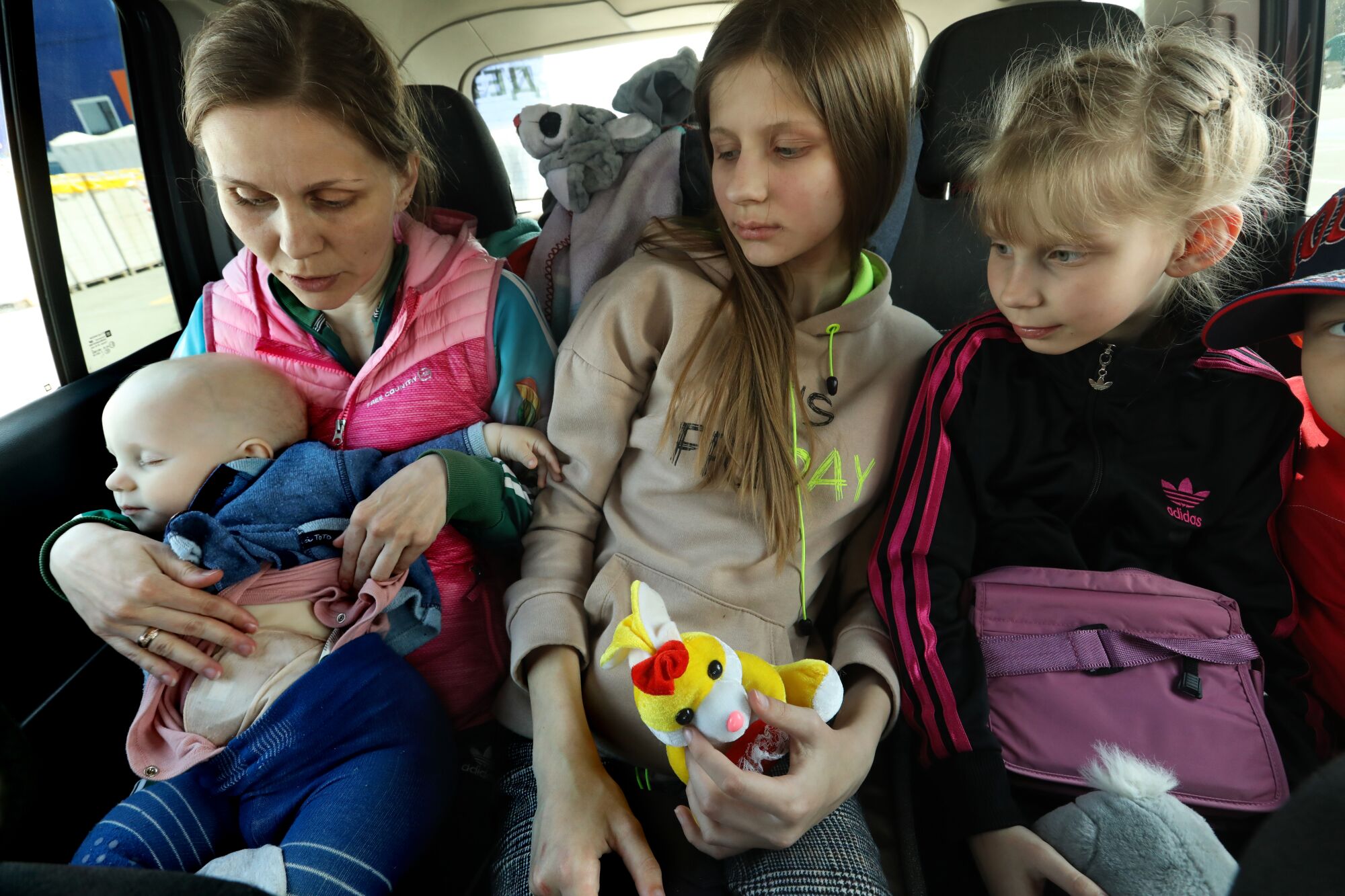  A woman in a car shows her baby's bandaged abdomen as two other children sit next to them, holding stuffed animals 