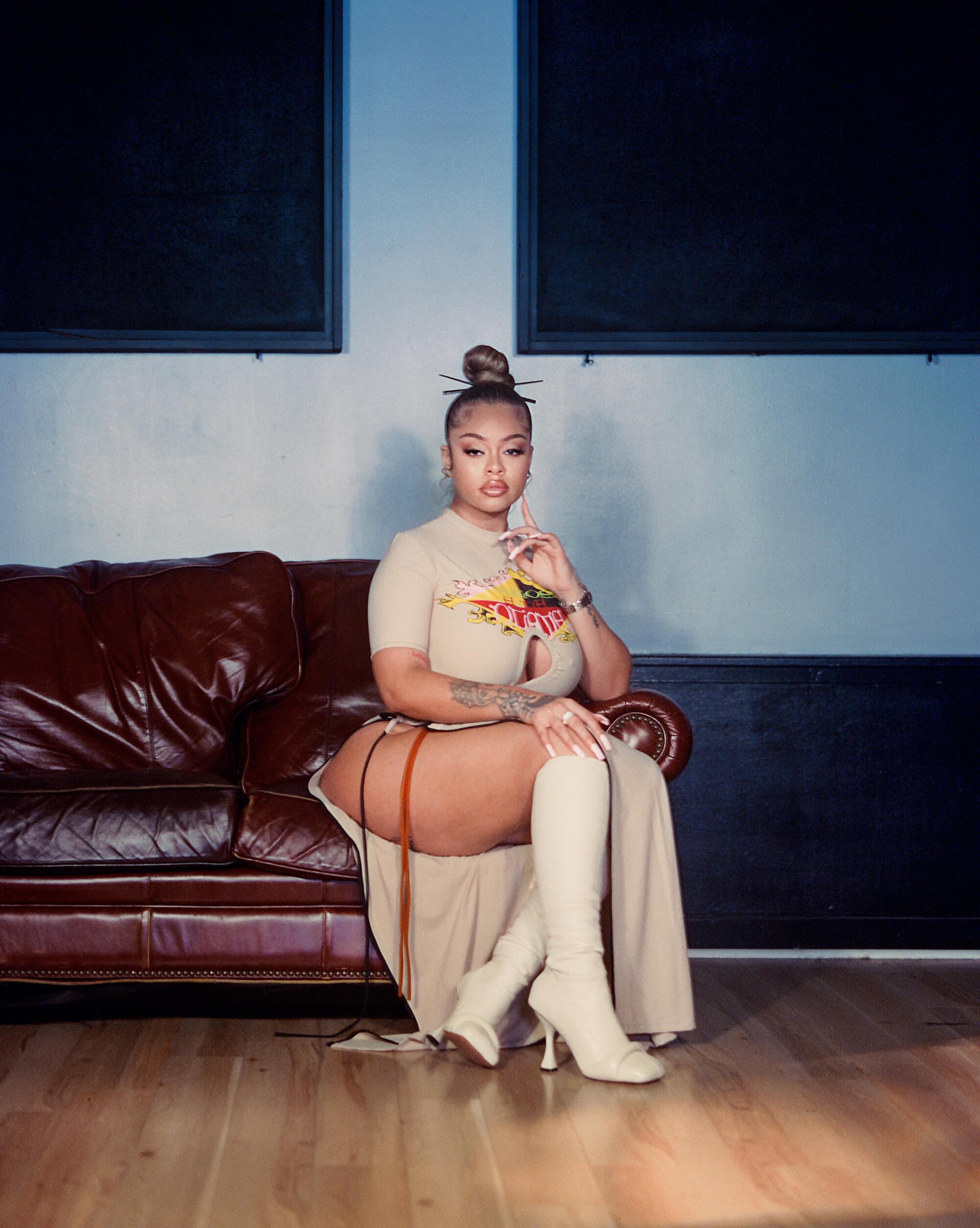 A female rapper sits on a burgundy sofa
