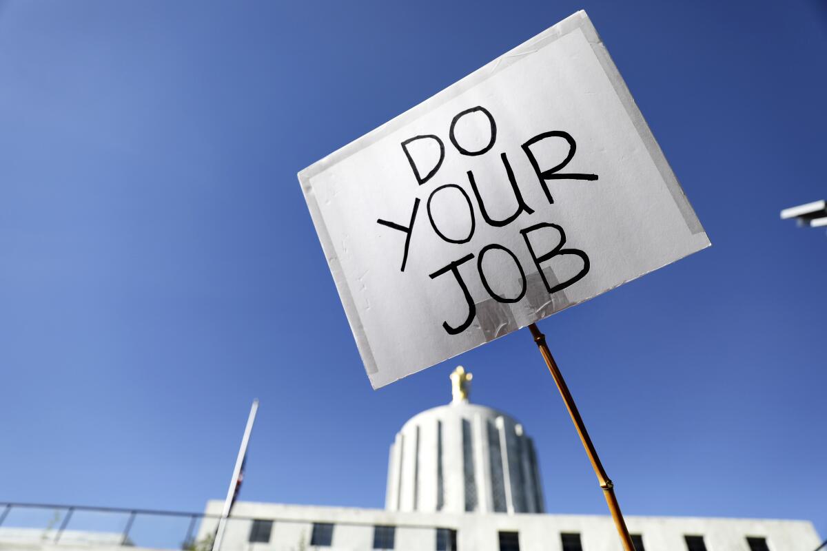 A picket sign that reads "Do Your Job" is displayed in front of the Oregon State Capitol 