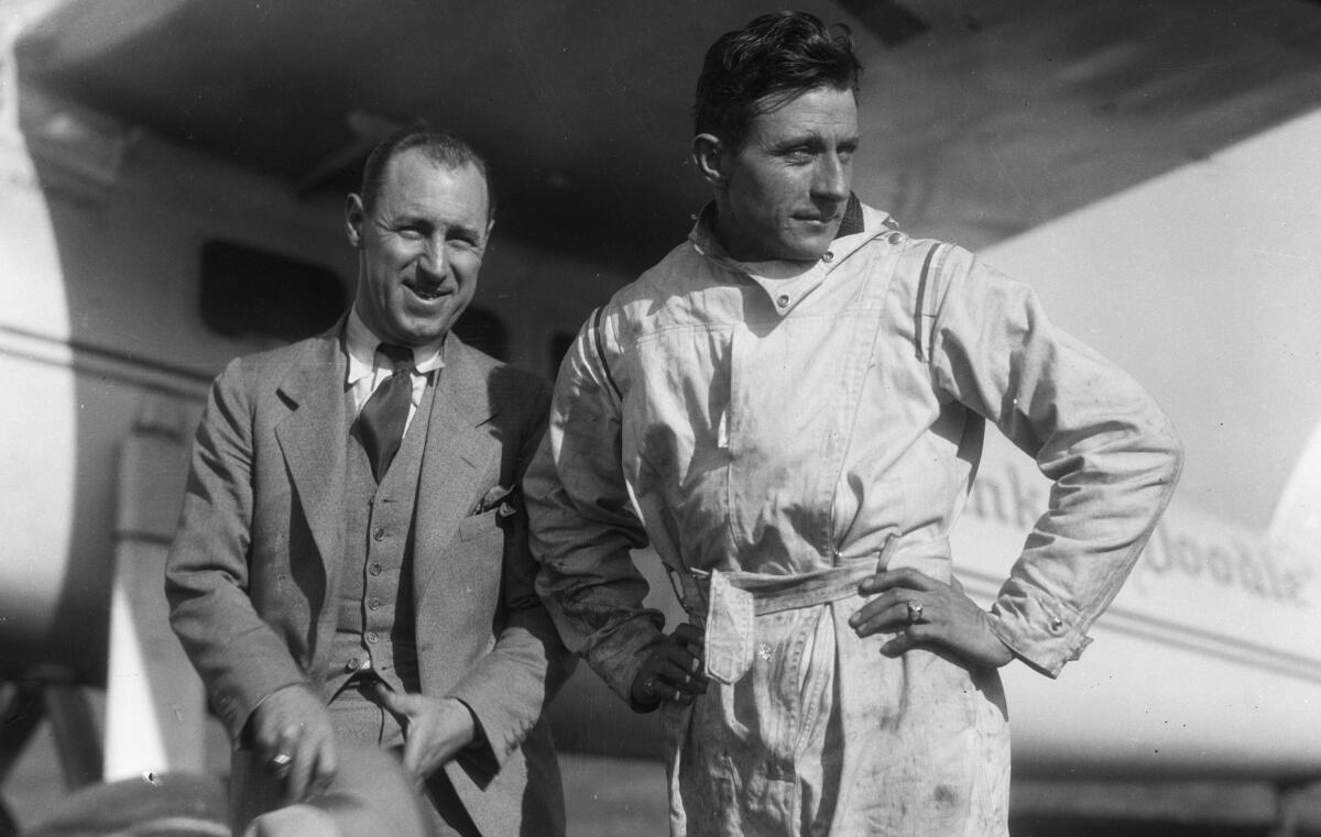 Two men stand near a small plane.