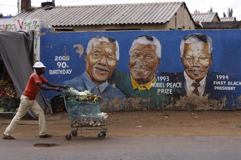 A South African hawker pushes his cart past portraits of the late former President Nelson Mandela at various stages of his life painted on a wall the Johannesburg suburb of Soweto.
