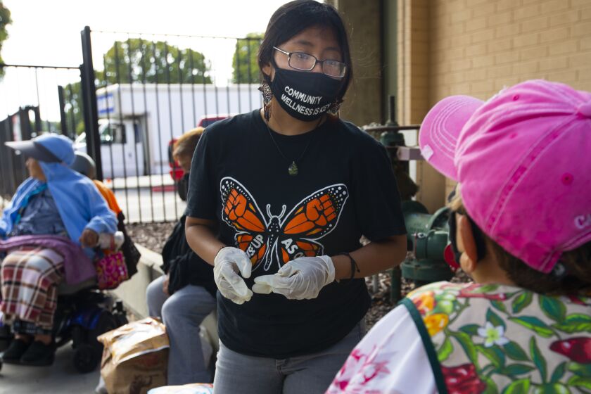 OXNARD, CA - JULY 19: Beatriz Basurto, 19, middle, of Oxnard hands food to Josefa Hernandez, right, age 70, at a food give away on Sunday, July 19, 2020 in Oxnard, CA during the coronavirus pandemic. Several organizations distributed food to mostly local farm workers and their families. Seniors arrived via scooters asking for food. Beatriz Reyes is part of a new generation of immigrants who are eligible for DACA - but left in the dark as Trump tries to end DACA again and refuses to take new applications despite SCOTUS ruling. (Francine Orr / Los Angeles Times)