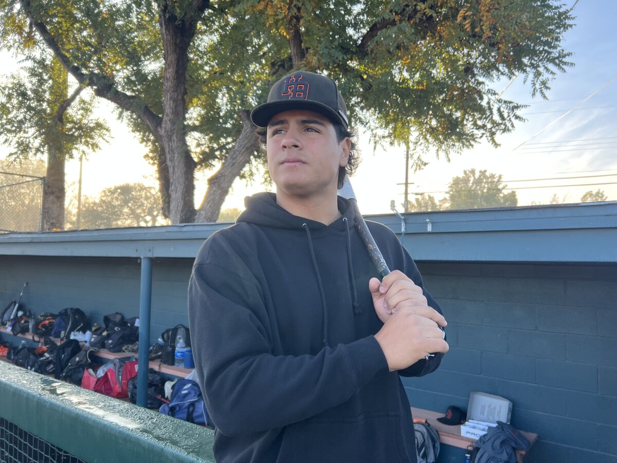Ralphy Velazquez of Huntington Beach High holds a bat near the dugout.
