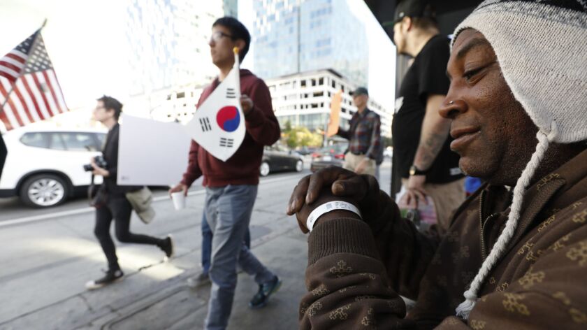 Lee Jones, 54, right, is a homeless man waiting at the bus stop watching a demonstration by multiple groups in favor of the proposed Koreatown homeless shelter, on May 26.