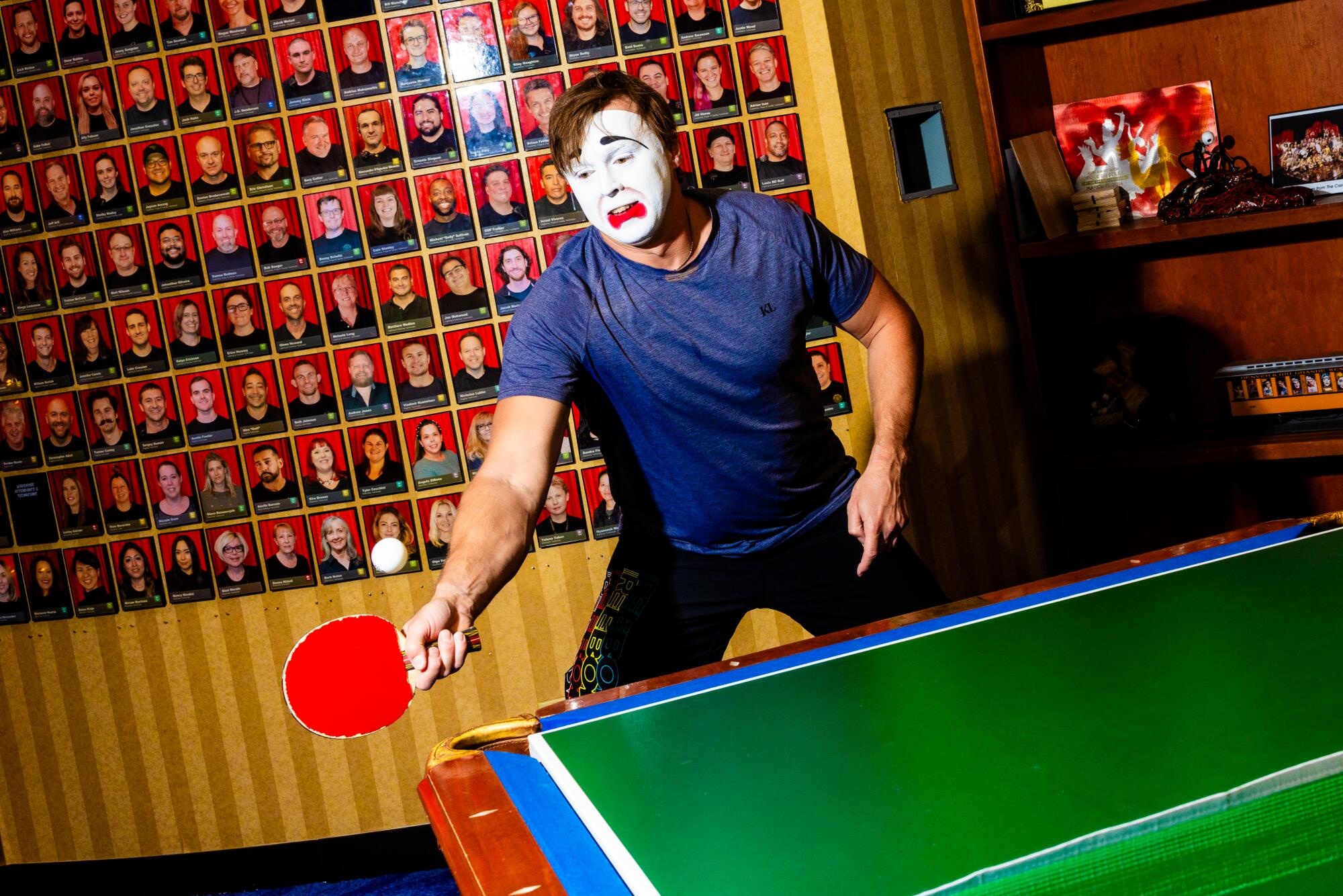 A man in clown makeup plays ping-pong backstage.