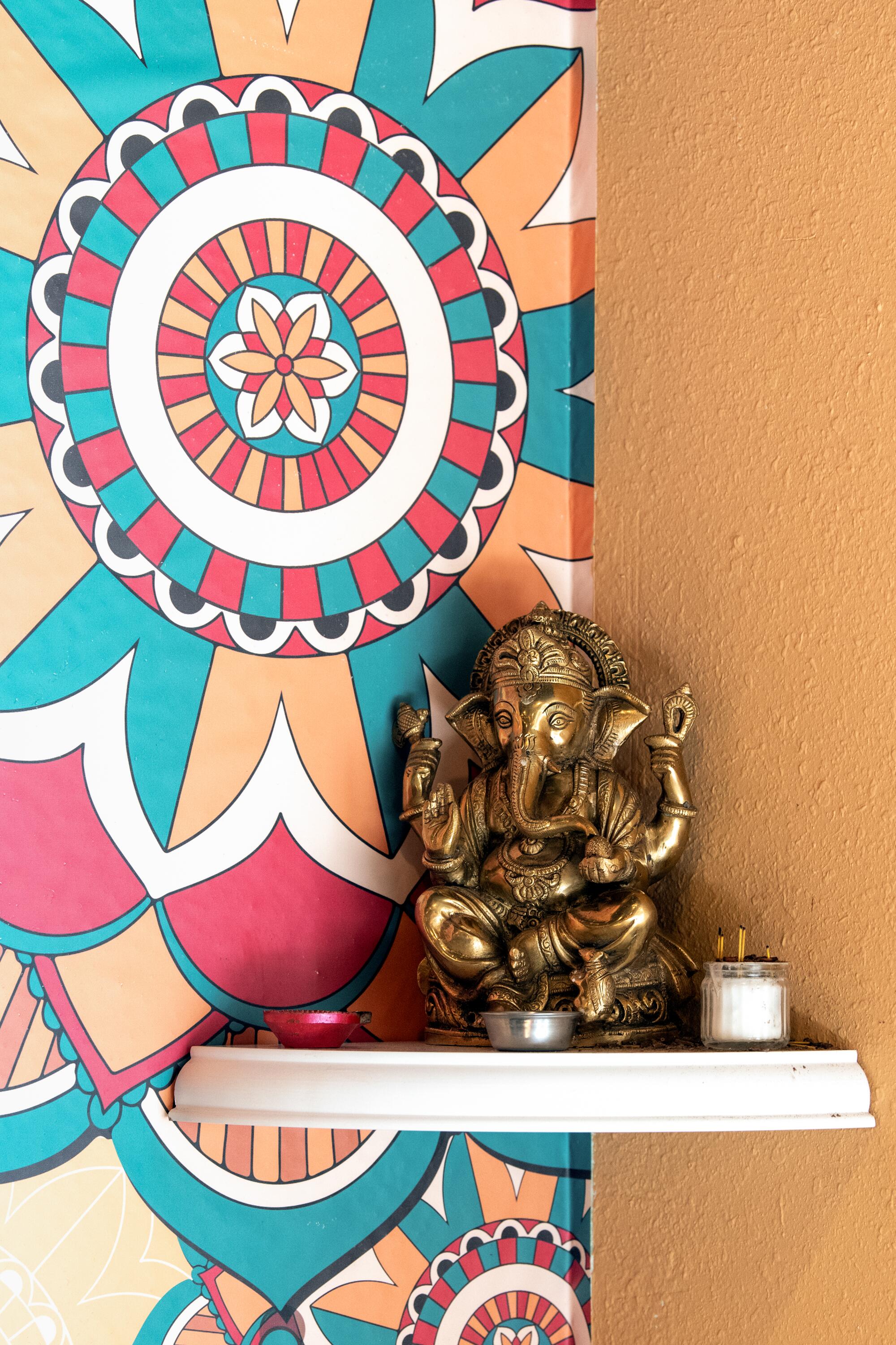 A statue of Ganesha on a corner shelf in front of a colorful patterned wall