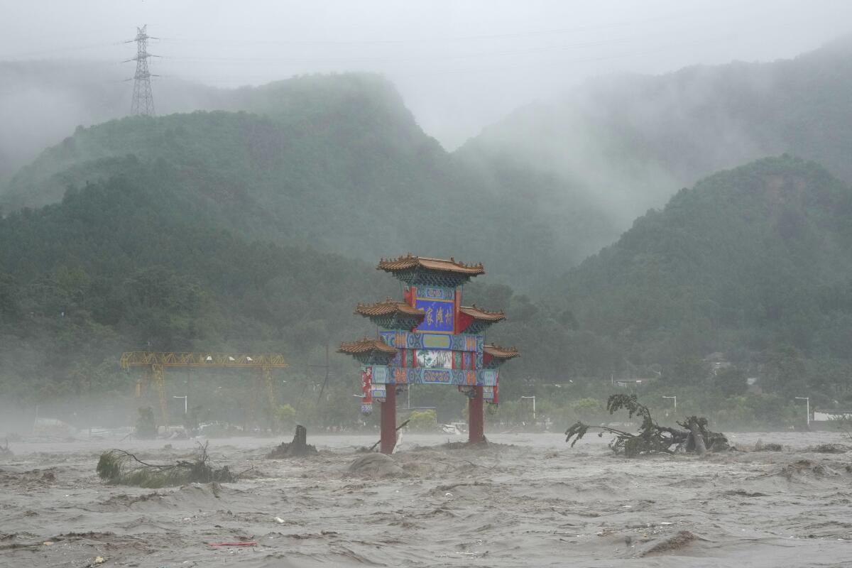 A traditional gate is surrounded by floodwaters with hills in the distance. 