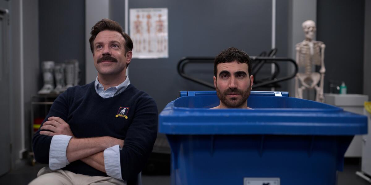 Jason Sudeikis and Brett Goldstein, one in a chair, the other in a trash bin, sit next to each other in "Ted Lasso."