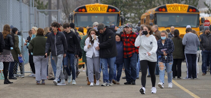 Parents walk away with their kids from the Meijer's parking lot, where many students gathered following an active shooter situation at Oxford High School, Tuesday, Nov. 30, 2021, in Oxford, Mich. Police took a suspected shooter into custody and there were multiple victims, the Oakland County Sheriff's office said. (Eric Seals/Detroit Free Press via AP)