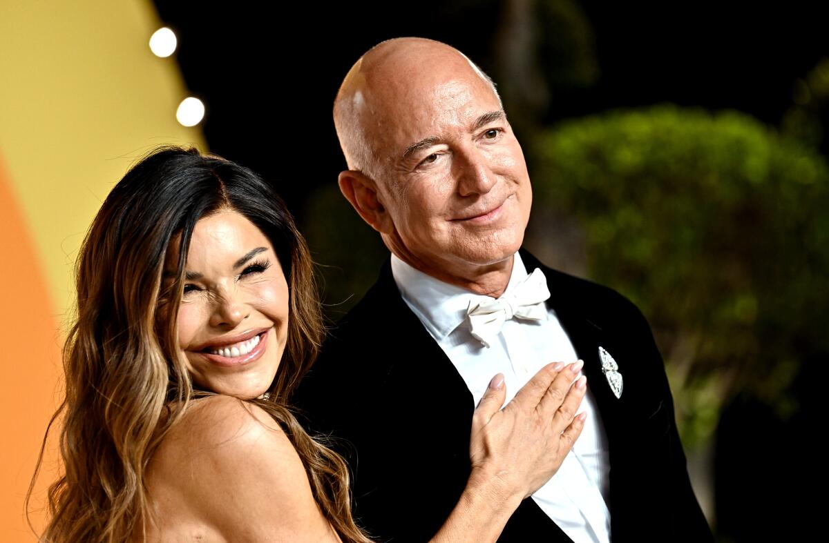 Lauren Sanchez smiles broadly while placing one hand on the chest of a tuxedo-clad Jeff Bezos