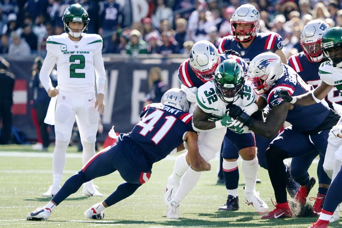 New York Jets running back Michael Carter (32) tries to break free from the New England Patriots during the first half of an NFL football game, Sunday, Oct. 24, 2021, in Foxborough, Mass. At left is New York Jets quarterback Zach Wilson (2). (AP Photo/Mary Schwalm)