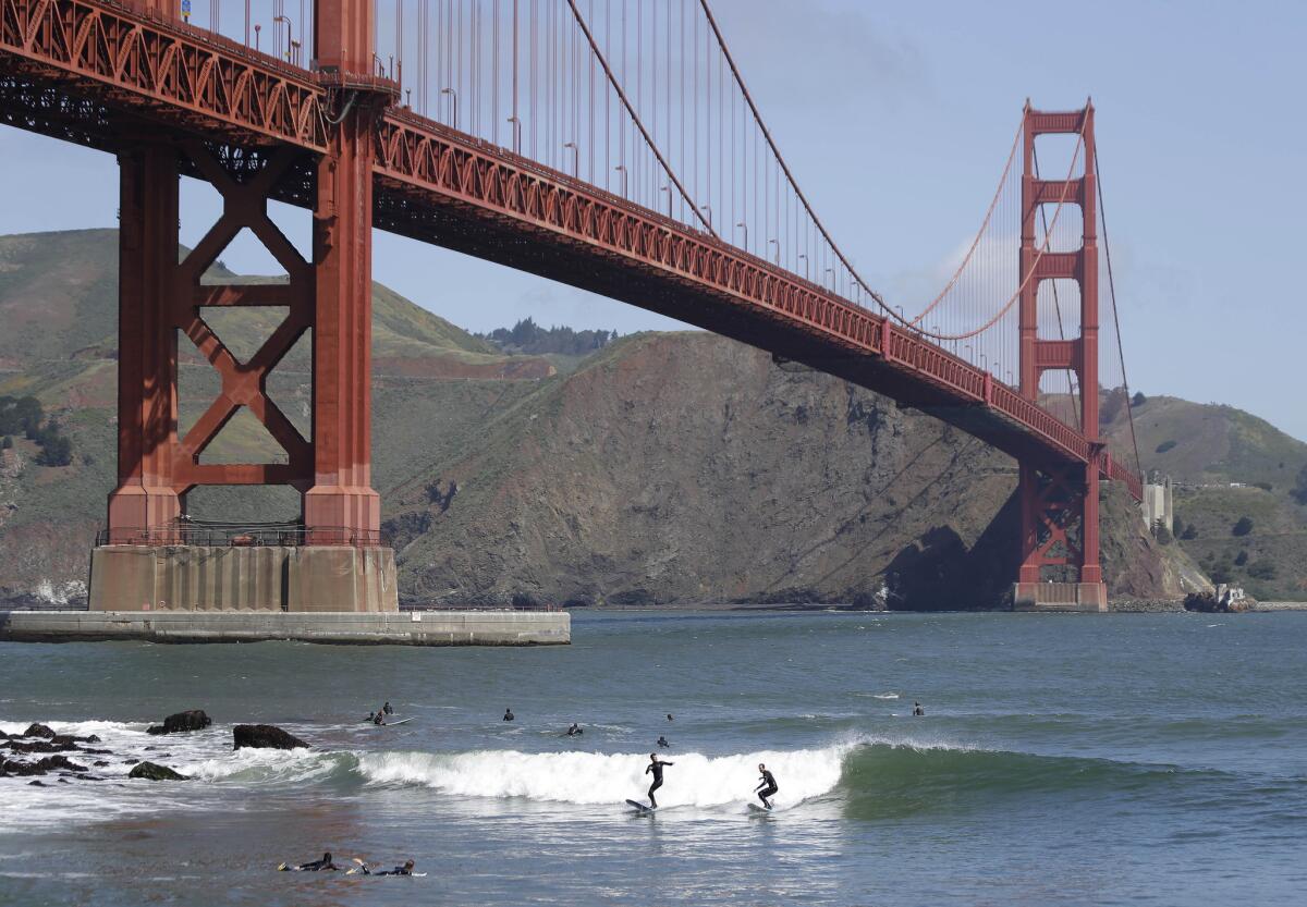 Two surfers ride a wave below the Golden Gate Bridge in San Francisco.