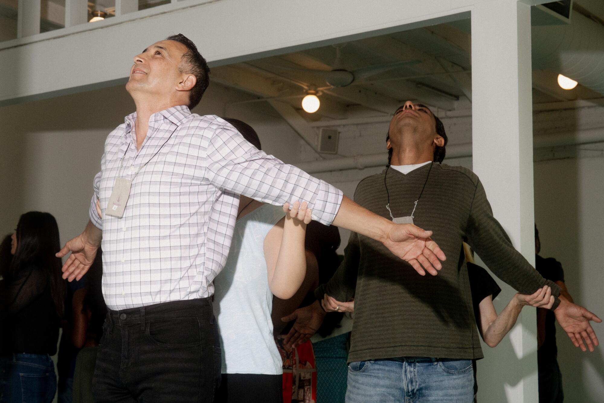 Two standing men stretch their arms backward as women stand behind them